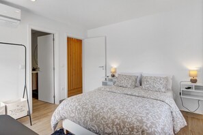 A bedroom with a bed, bedside tables, a wardrobe, and an air conditioning unit.