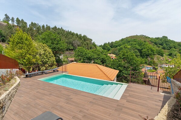 A swimming pool on a wooden deck with a view of a hillside and houses.