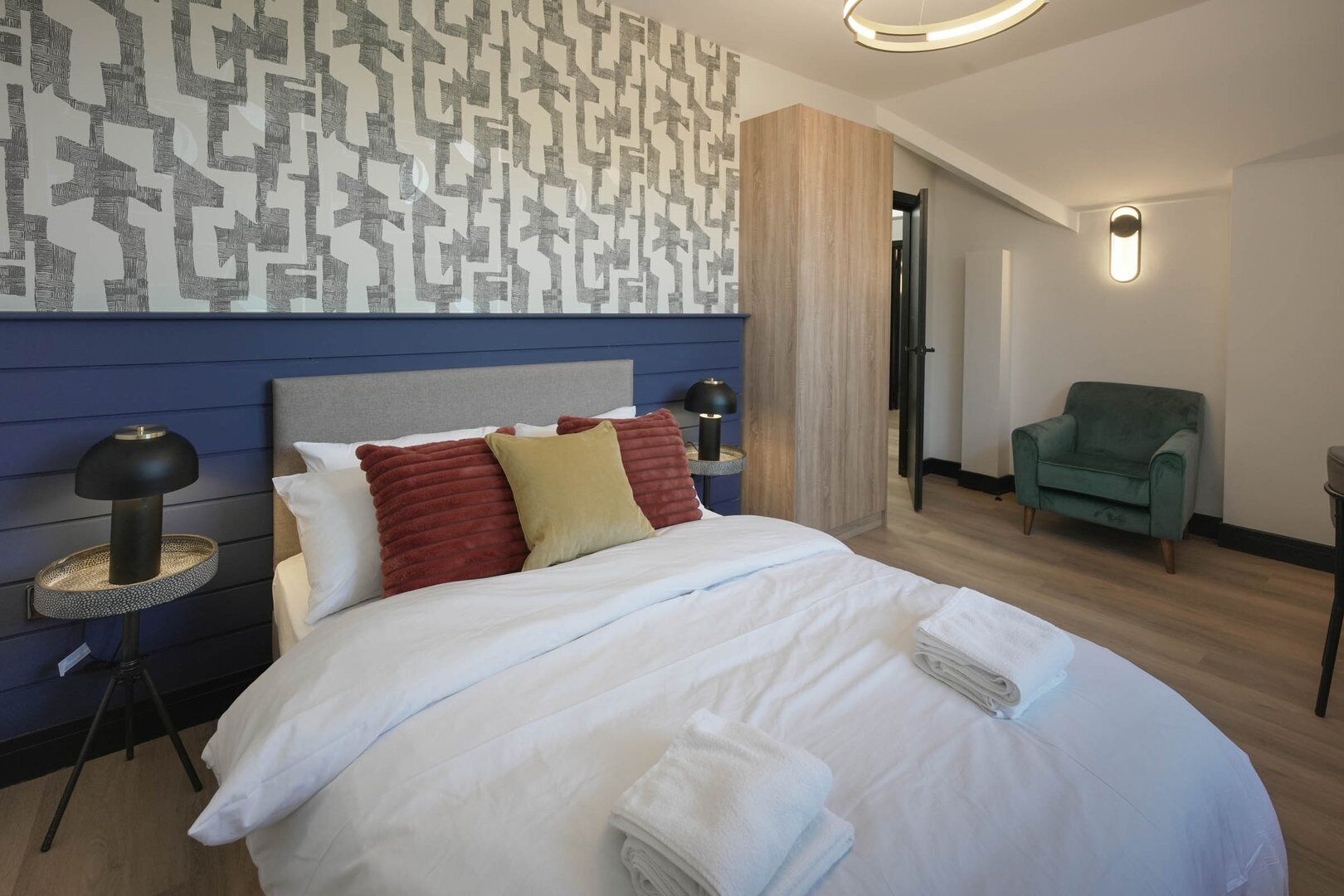 Una moderna camera d'hotel con un letto grande, due lampade ai lati del letto, una poltrona verde e una parete decorata.
