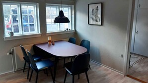A dining area with a table and chairs, a pendant light, a radiator, and a window with a view of parked cars.