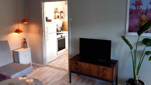 A modern living room with a sofa, a coffee table, a TV on a wooden stand, and a potted plant.