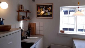 A kitchen with a stove, sink, and window. There is a poster on the wall and a shelf with kitchen items.