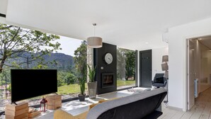 En moderne stue med et fladskærms-TV, en pejs og et stort vindue med udsigt til et bjergrigt landskab.