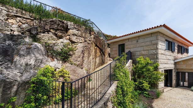 Un edificio de piedra con techo de tejas rojas, una escalera de piedra que conduce a un balcón y un patio empedrado.