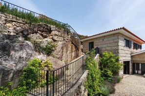 Un edificio de piedra con techo de tejas rojas, una escalera de piedra que conduce a un balcón y un patio empedrado.