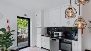 Una cocina moderna con armarios blancos, un microondas, estufa y una encimera negra. Hay lámparas geométricas colgantes y un extintor en la pared.