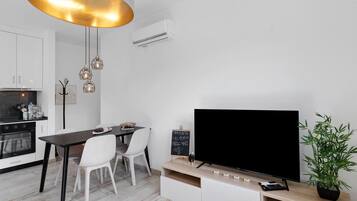Una cocina moderna con armarios blancos, una mesa de comedor con sillas, un televisor negro sobre un mueble de madera y una planta en maceta.