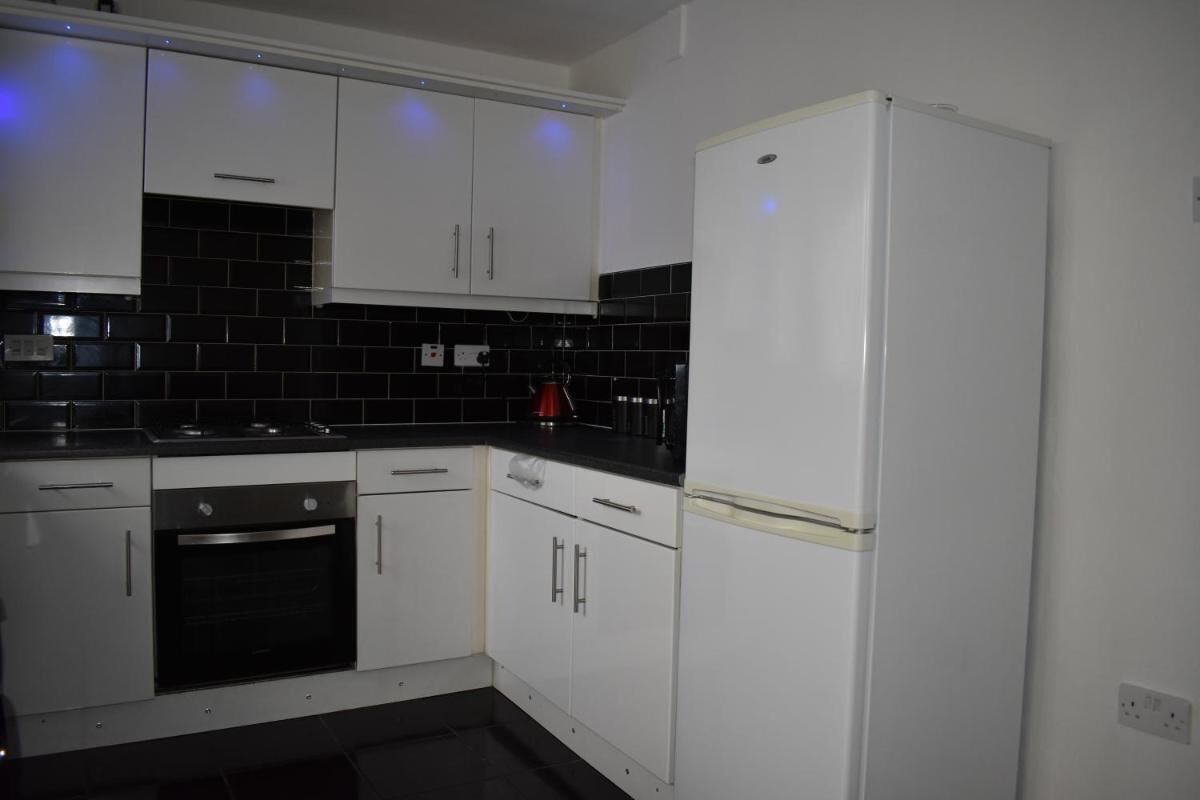 A modern kitchen with white cabinets, a black tiled backsplash, and a white refrigerator.