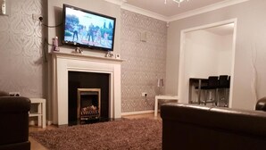A living room with a fireplace, a television mounted above it, and a sofa. - Charming Liverpool Home With Gardens and Parking (Liverpool)