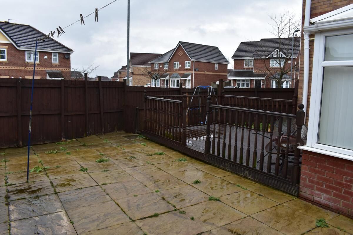 A residential backyard with a paved patio, a wooden fence, and houses in the background.