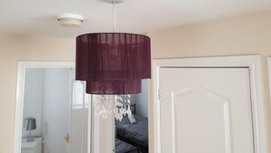 A room with a hanging pendant light, a door, and a glimpse of a bed with a gray blanket. - Charming Liverpool Home With Gardens and Parking (Liverpool)