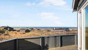 Una terraza de madera con vista a la playa y casas a lo lejos.