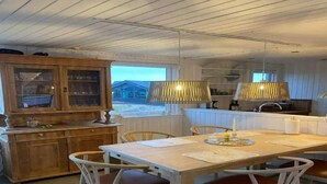 Un comedor con mesa y sillas de madera, un armario con puertas de vidrio y dos lámparas colgantes.