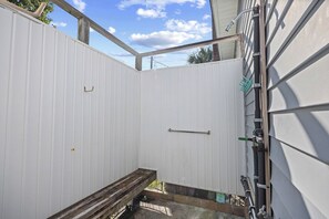 A narrow outdoor space with a wooden bench, a metal handrail, and a white wall. - 3 Bedroom Home| Steps 2 Beach| Pet Friendly (North Myrtle Beach)