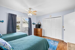 Een slaapkamer met twee bedden, een plafondventilator, een dressoir, een televisie en een grote kledingkast.