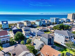 Een kustwoongebied met meerdere twee-onder-een-kapwoningen, een strand op de achtergrond en een heldere lucht.