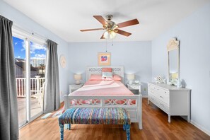 A bedroom with a bed, bedside tables, a bench, a ceiling fan, a window with curtains, and a view of the outside. - 3 Bedroom Home| Steps 2 Beach| Pet Friendly (North Myrtle Beach)