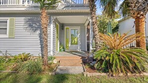 Una casa a due piani con un portico, palme e un vialetto in mattoni che conduce alla porta.