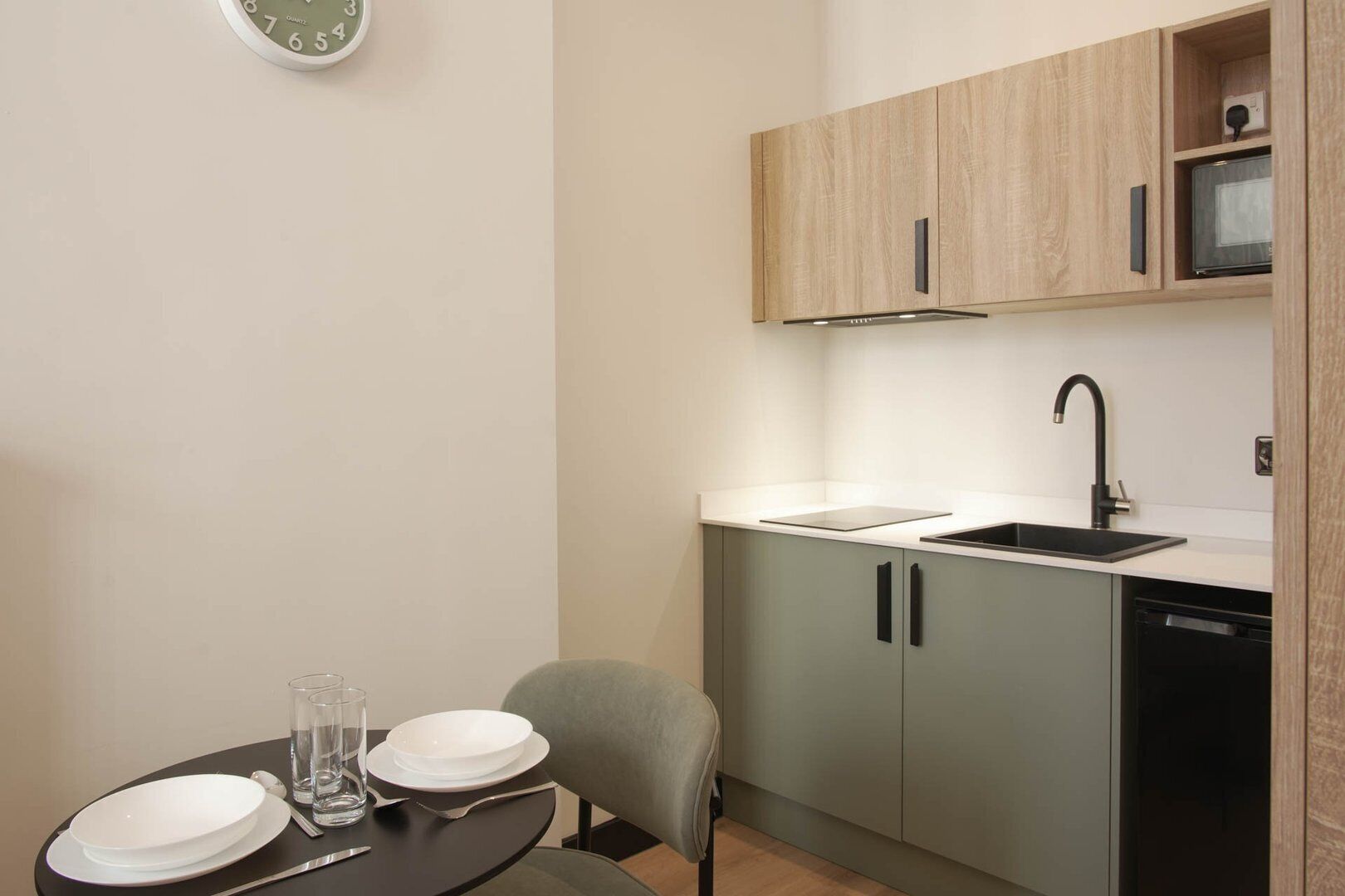 Una cocina compacta con un lavamanos, armarios y un reloj en la pared.