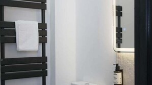 Een moderne badkamer met een zwarte handdoekhouder, een wit toilet en een rond wastafel met een spiegel erboven.