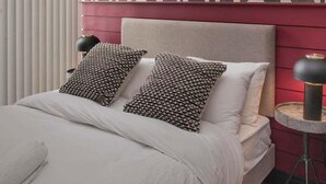 Een moderne slaapkamer met een behang, een bed met veel kussens en een klein nachtkastje met een lamp.