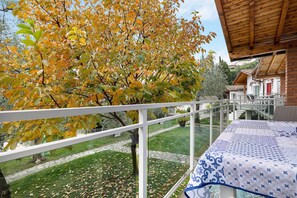 Un balcon donnant sur un arbre aux feuilles jaunes, une pelouse verdoyante et un bâtiment avec une porte rouge.