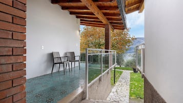 Un'area esterna coperta con un muro in mattoni, un parapetto in vetro e vista su un giardino e montagne.