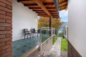 Un espacio al aire libre cubierto con pared de ladrillo, barandilla de vidrio y vistas a un jardín y montañas.
