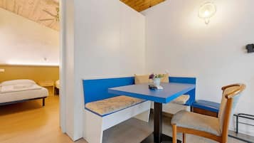 A room with a bed, a blue bench, a wooden chair, a table, and a ceiling fan.