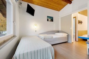 Une chambre à coucher comprenant un lit, une table de chevet, une fenêtre, un téléviseur fixé au mur et un tableau.