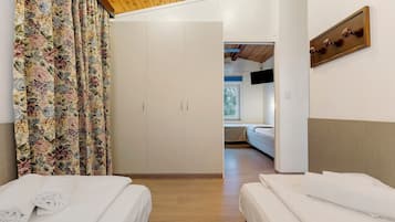Camera d'albergo con due letti, un armadio, una televisione e un soffitto in legno.