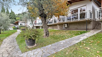 Un sentiero in pietra conduce a un edificio con un balcone, immerso tra alberi ed erba.
