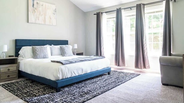 A bedroom with a bed, bedside tables, a nightstand, a window with curtains, and a painting on the wall.