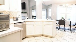 A modern kitchen with white cabinetry, a built-in microwave, and a dining area with a table and chairs.