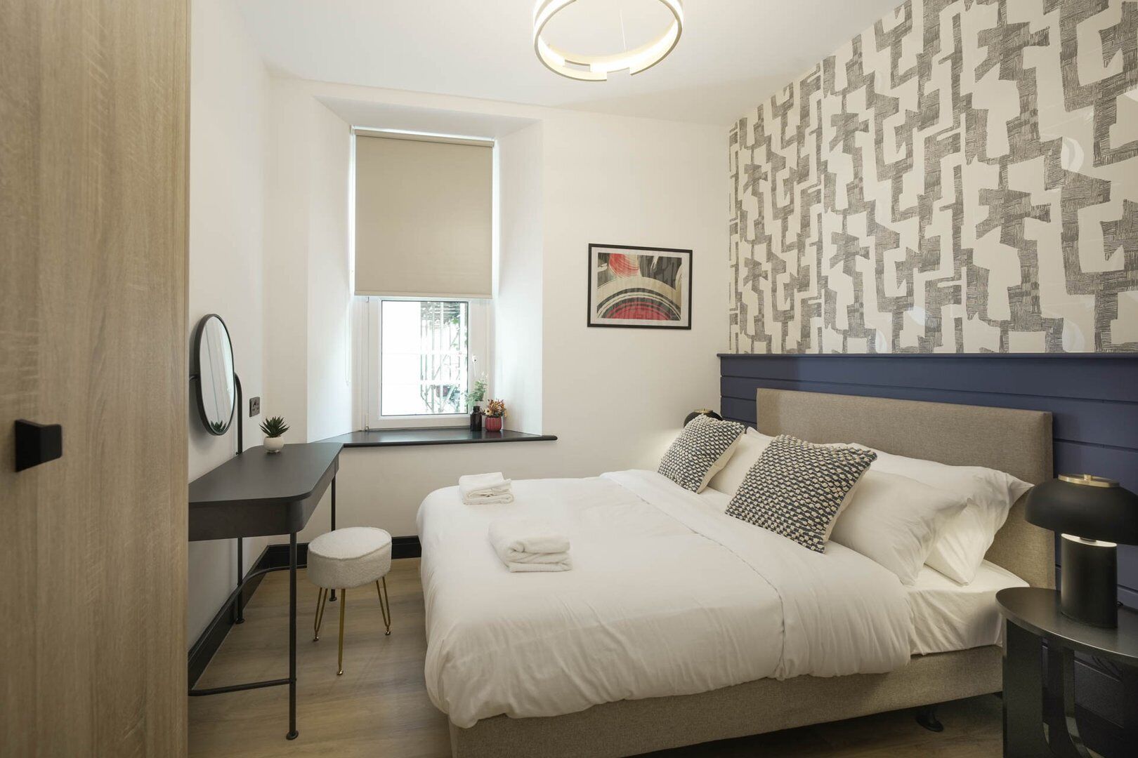 Camera d'albergo moderna con un letto, una scrivania, una sedia, una finestra e una parete con motivo geometrico.