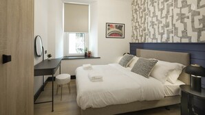 Une chambre d’hôtel moderne comprenant un lit, un bureau, une chaise, une fenêtre et un mur orné d’un motif géométrique.