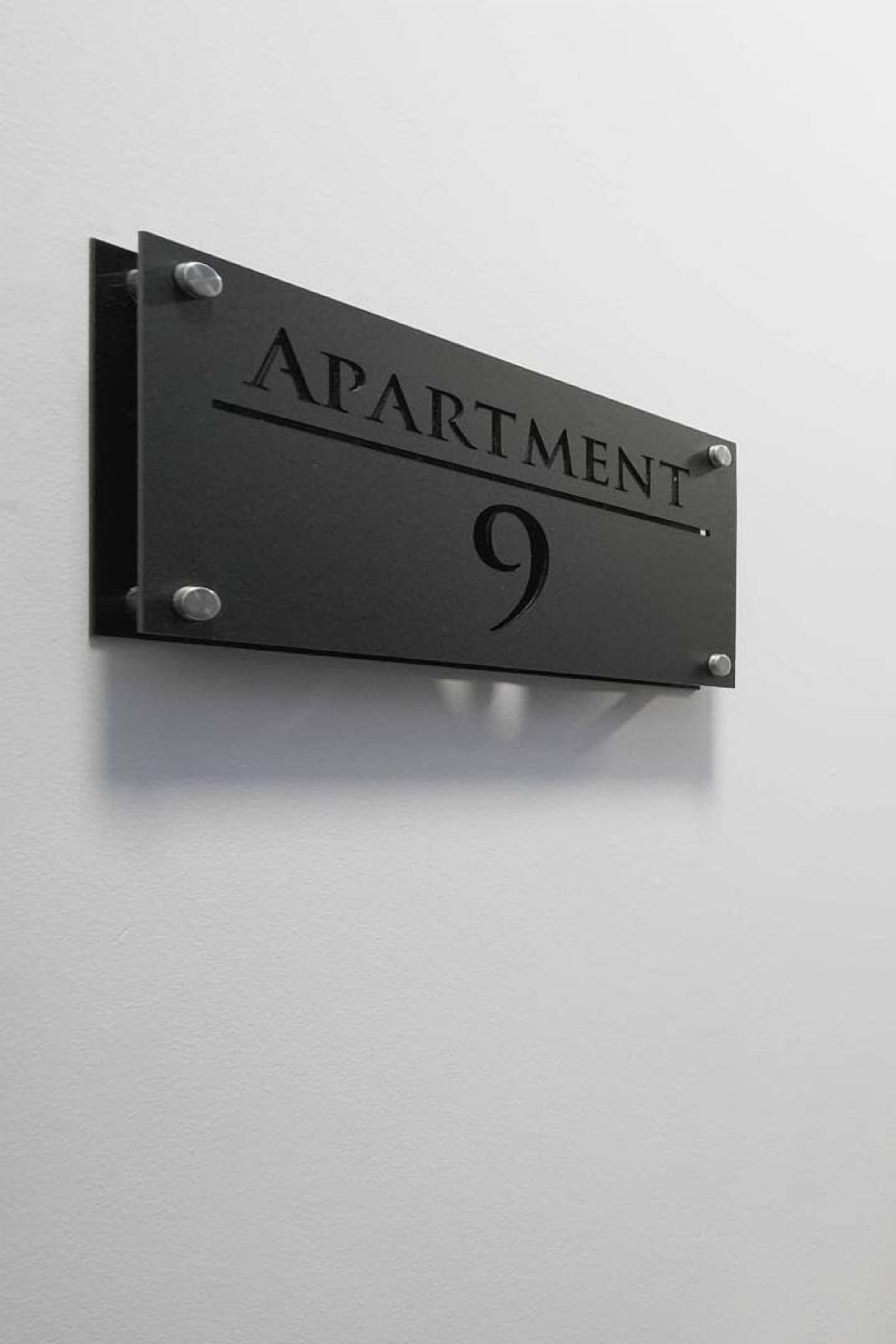 A black metal sign with the words "APARTMENT 9" mounted on a white wall.