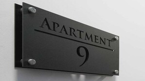 Une plaque en métal noir portant l’inscription « APPARTEMENT 9 », fixée à un mur blanc.