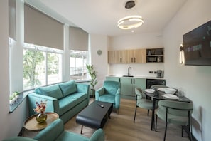 A modern living room with a sofa, coffee table, and a dining area with chairs. There is a kitchen with cabinets and appliances in the background. - Sixty Aparthotel 2bed, Central Cardiff + Parking (Cardiff)