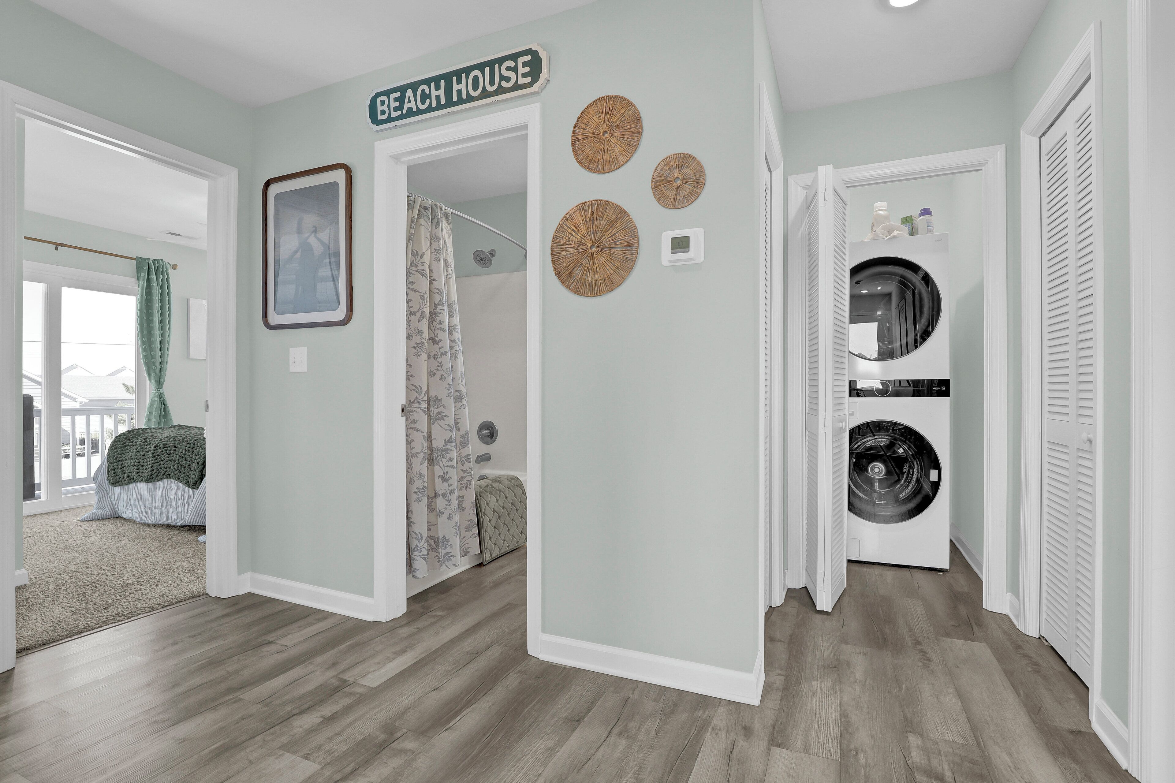 Een gang met een bord waarop ‘Beach House’ staat, een wasmachine en een doucheruimte.