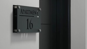 Egy fekete tábla, melyen a „16. LAKÁS” felirat szerepel, és egy falra van rögzítve.