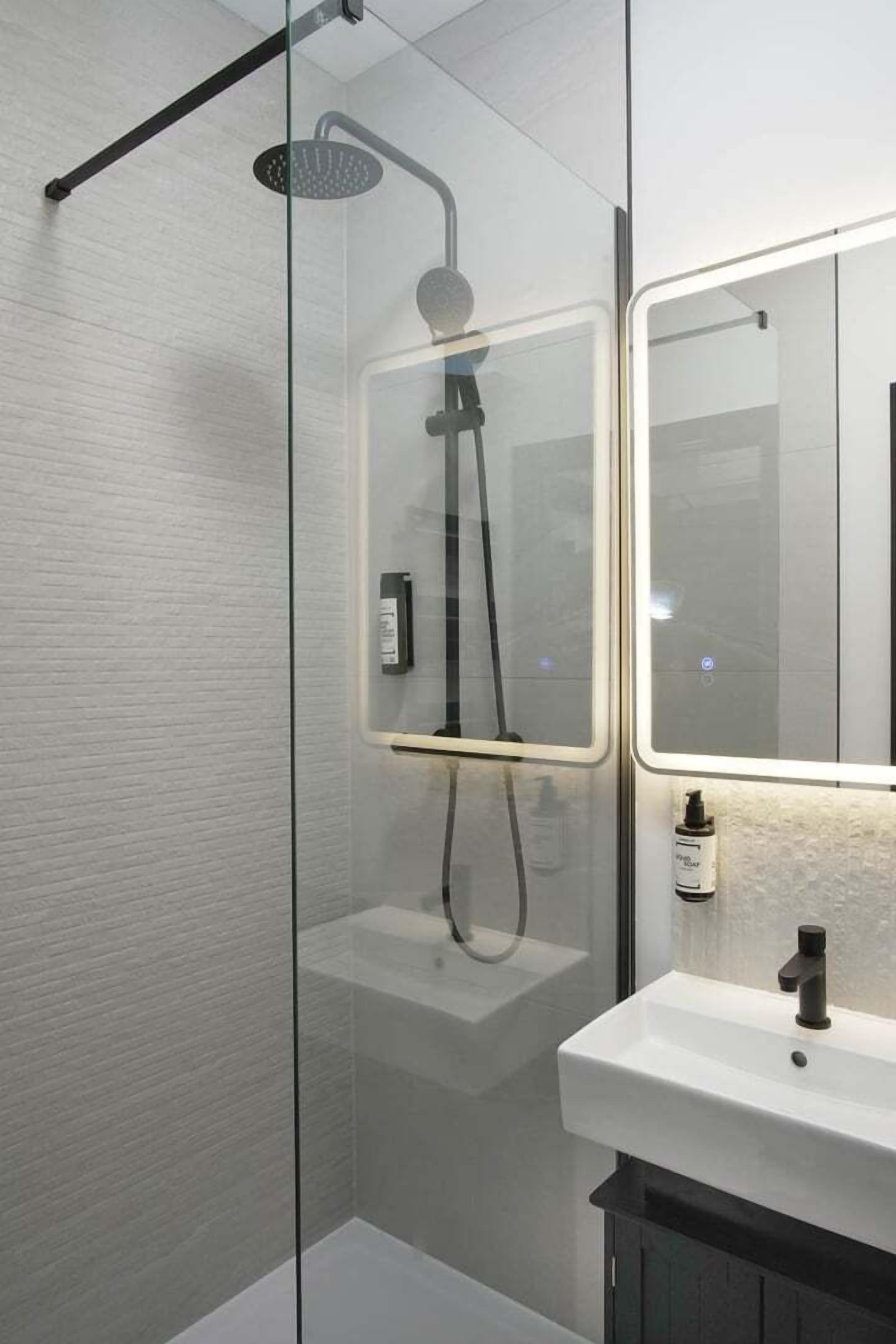 Ein modernes Badezimmer mit einer Duschkabine, einem weißen Waschbecken und einem Spiegel.