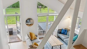 A spacious living area with a large window, a round mirror, a sofa with cushions, and a coffee table. - 4 Star Holiday Home in Dannemare (Dannemare)