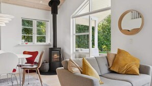 A modern living room with a grey sofa, red chairs, a black wood-burning stove, and large windows offering a view of greenery. - 4 Star Holiday Home in Dannemare (Dannemare)