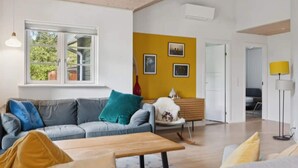 A modern living room with a grey sofa, a wooden coffee table, and a yellow wall with framed pictures. - 4 Star Holiday Home in Dannemare (Dannemare)