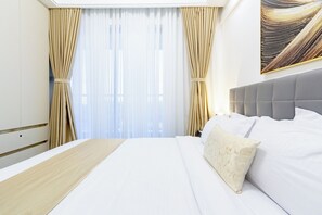 Habitación de hotel con una cama grande, cortinas color beige y un cuadro en la pared.