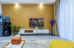 A modern living room with a flat-screen TV, a water dispenser, a fan, and a sofa.