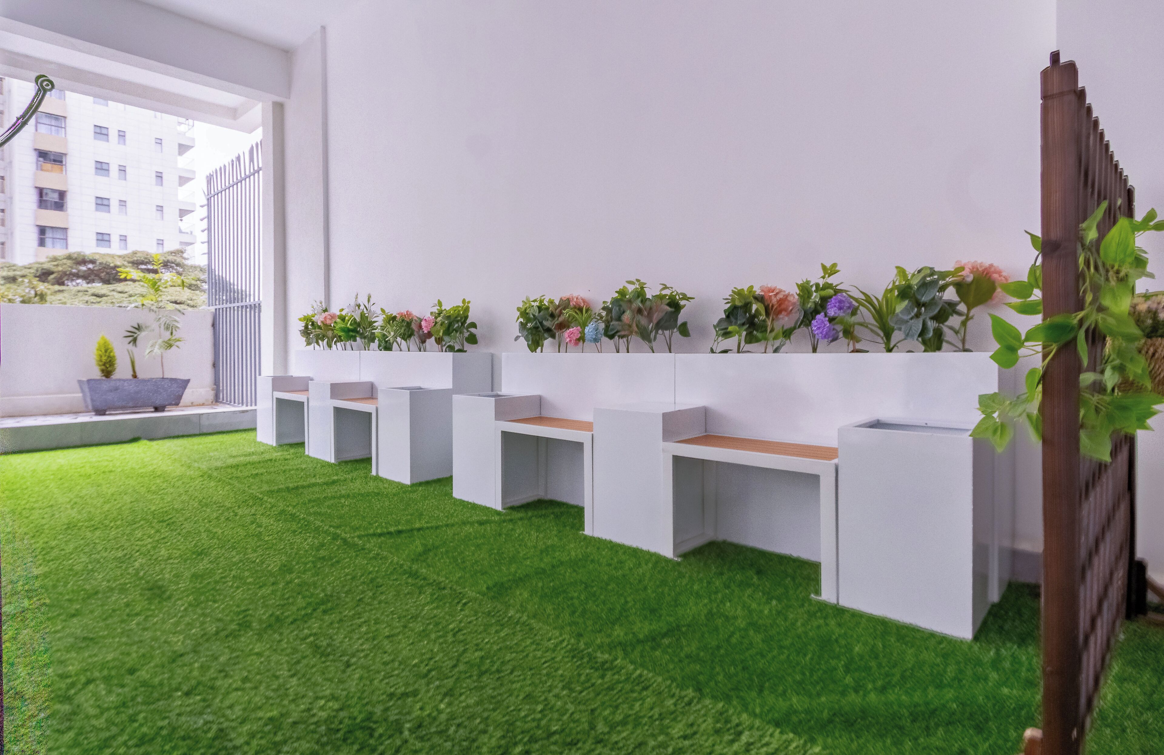 A modern interior with white walls, a green artificial grass floor, and a row of planters with flowers.