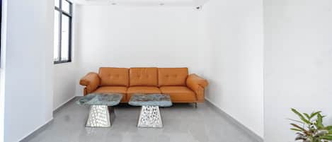 A modern interior with a sofa and two matching tables, a potted plant, and a large window.