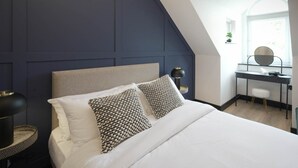 A modern bedroom with a large bed, two patterned pillows, a desk with a chair, and a window with natural light. - Sixty Aparthotel 2bed, Central Cardiff + Parking (Cardiff)